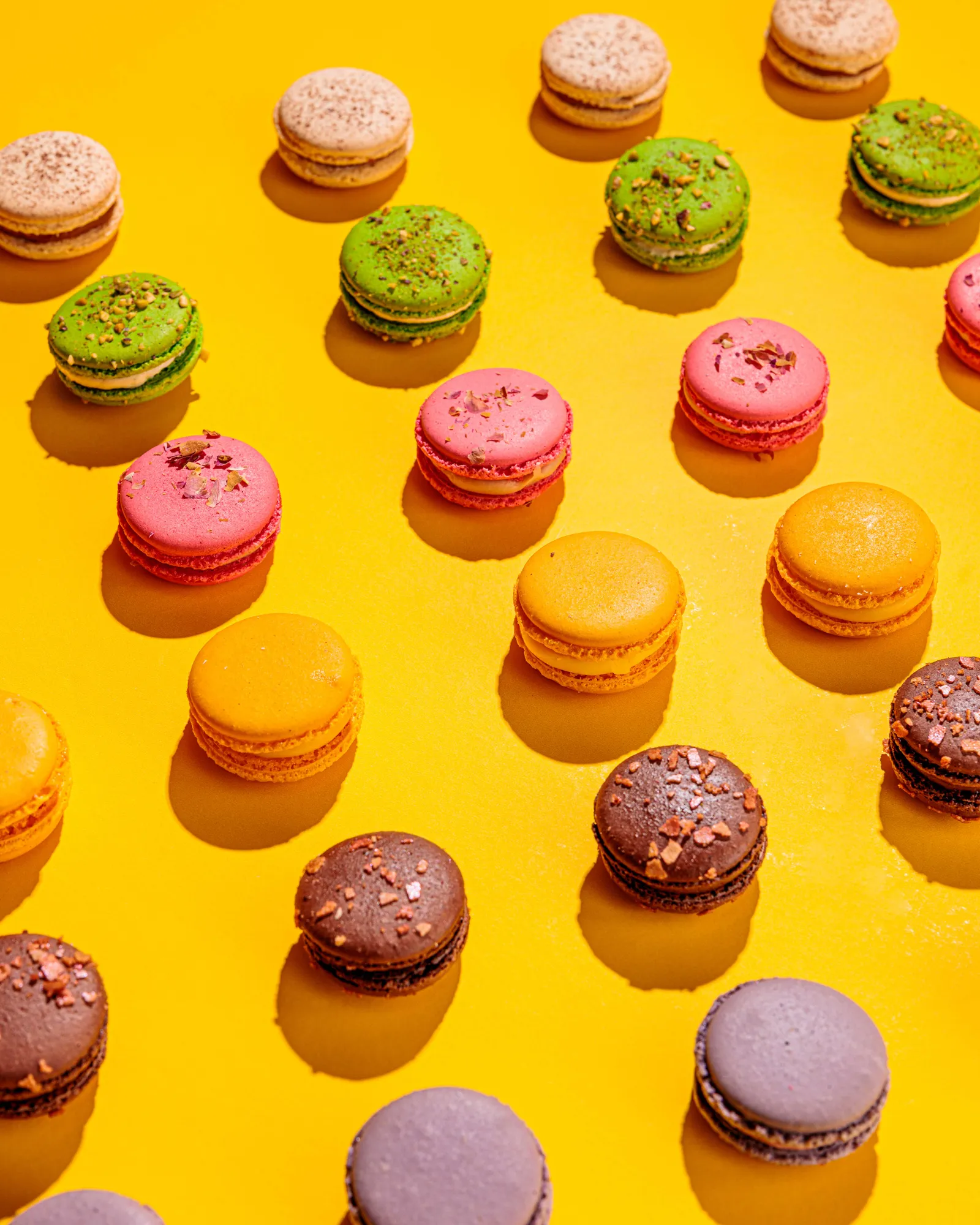 Rows of colourful macarons on a yellow background