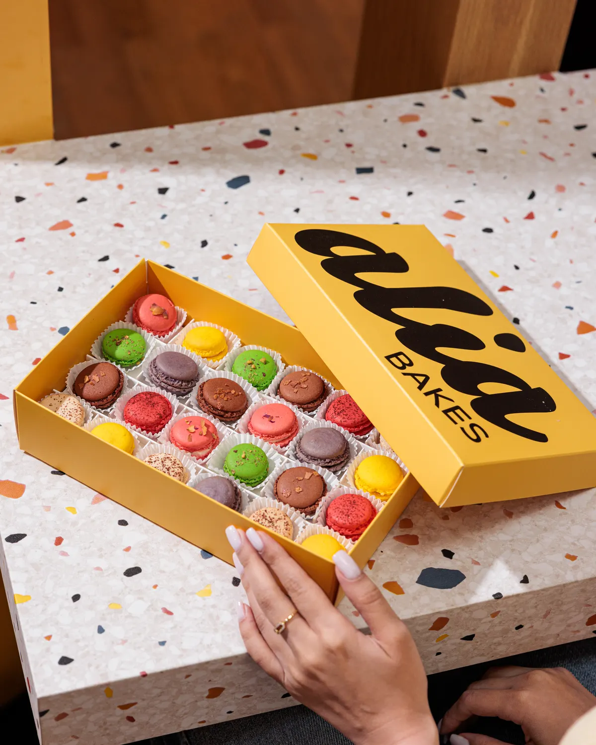 An open yellow alia box of macarons